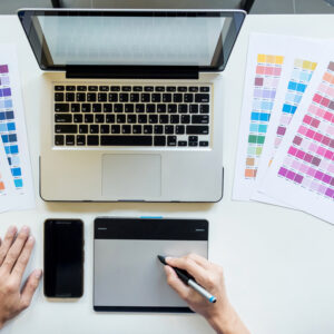 Top view of a young graphic designer working on a desktop computer and using some color swatches, top view.